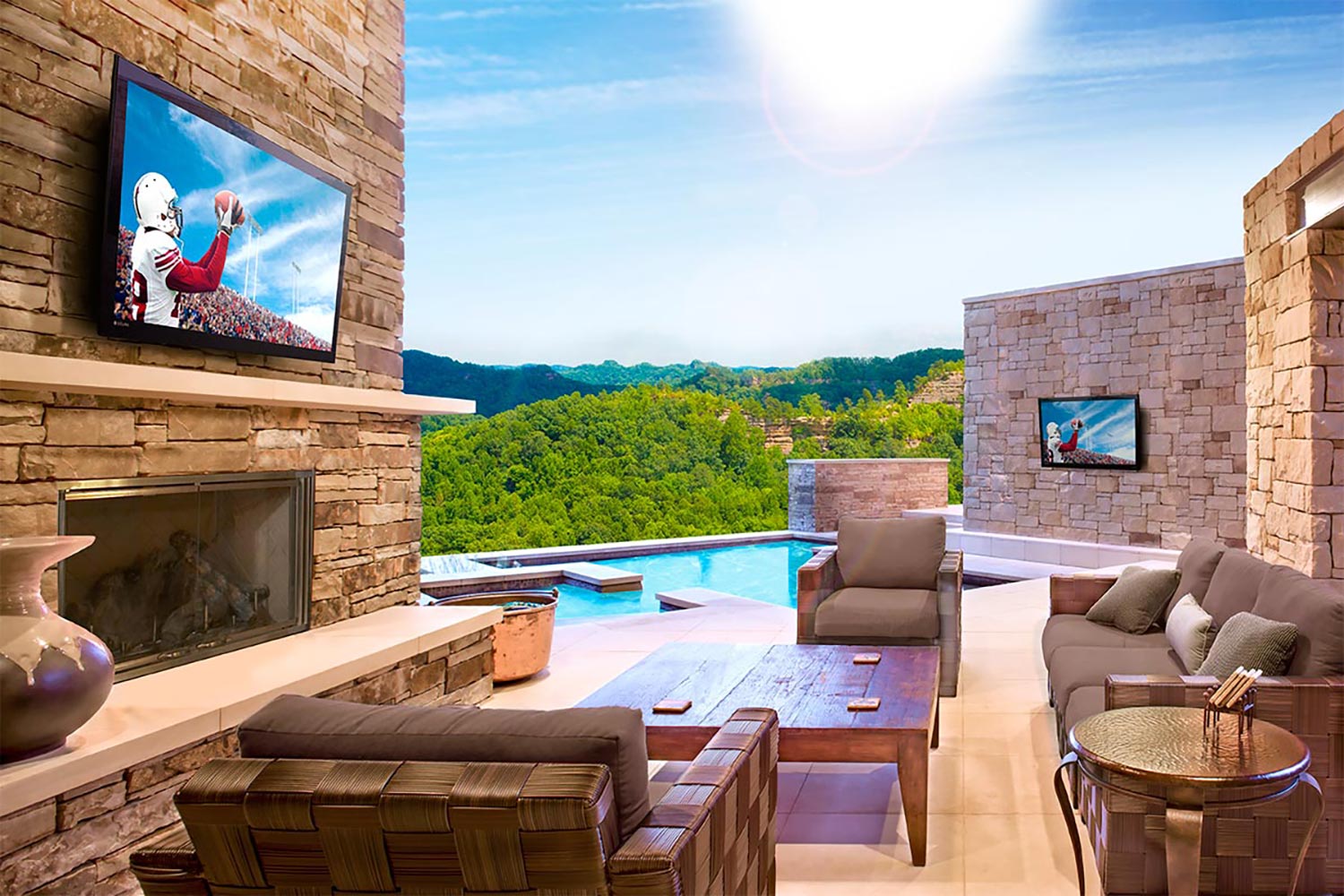Outdoor lounge with stone walls, TVs, fireplace, and a pool with scenic view