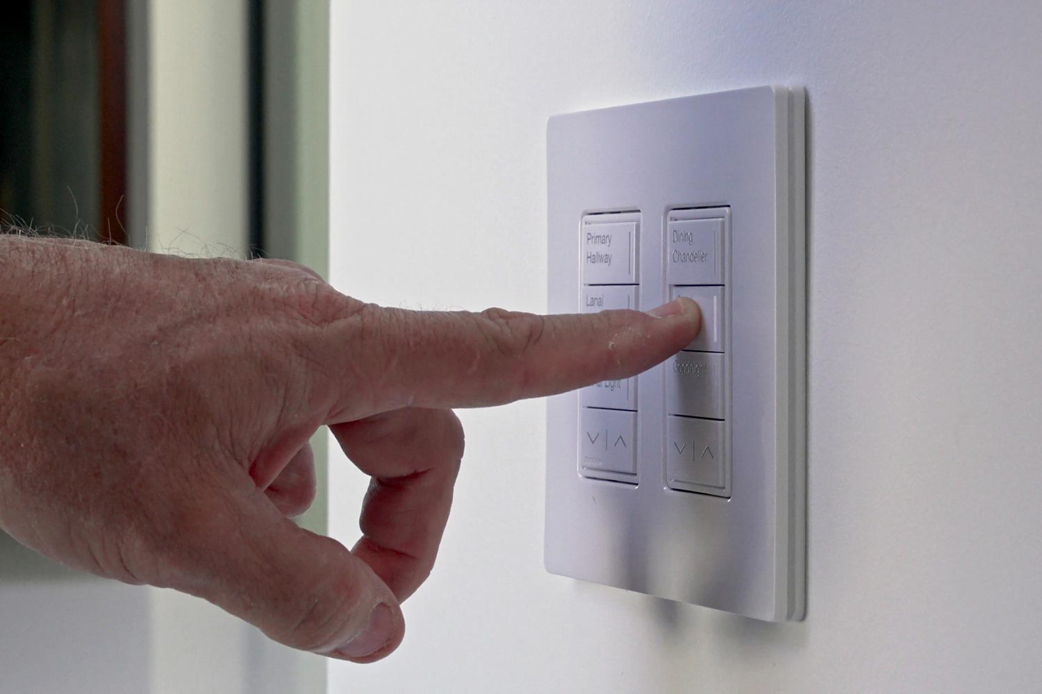 Person pressing a wall-mounted smart switch labeled for lighting scenes