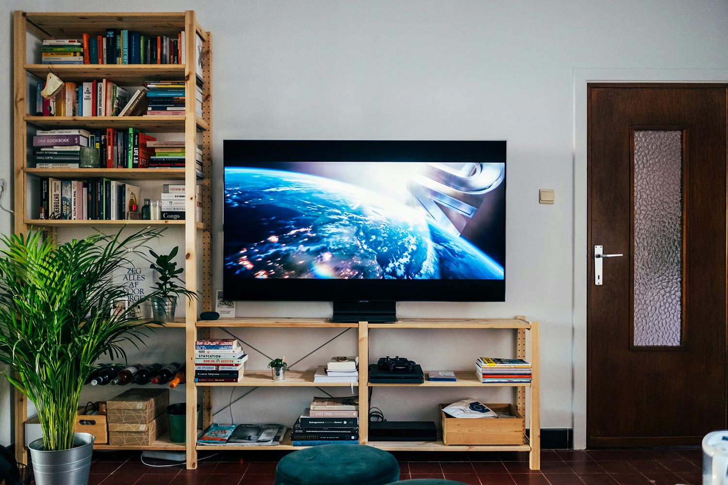 Wall-mounted TV in living room playing a movie with bookshelves and plants