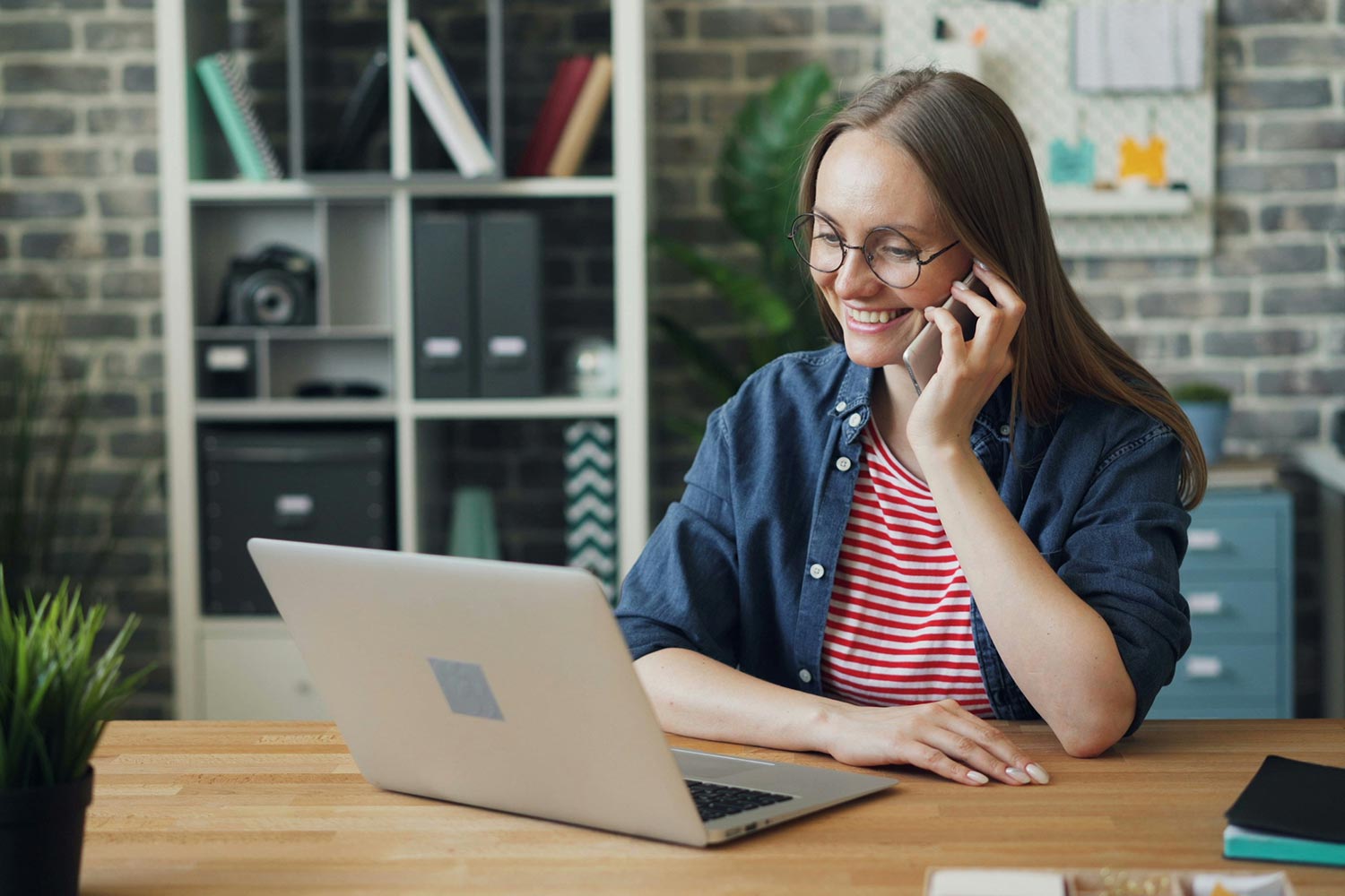 Woman smiling during phone call at desk with laptop in cozy home office
