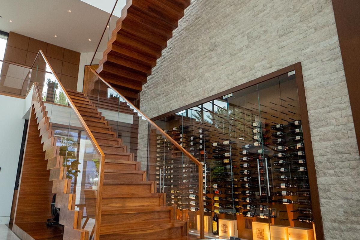 Floating wooden staircase beside a glass wine cellar in a modern home