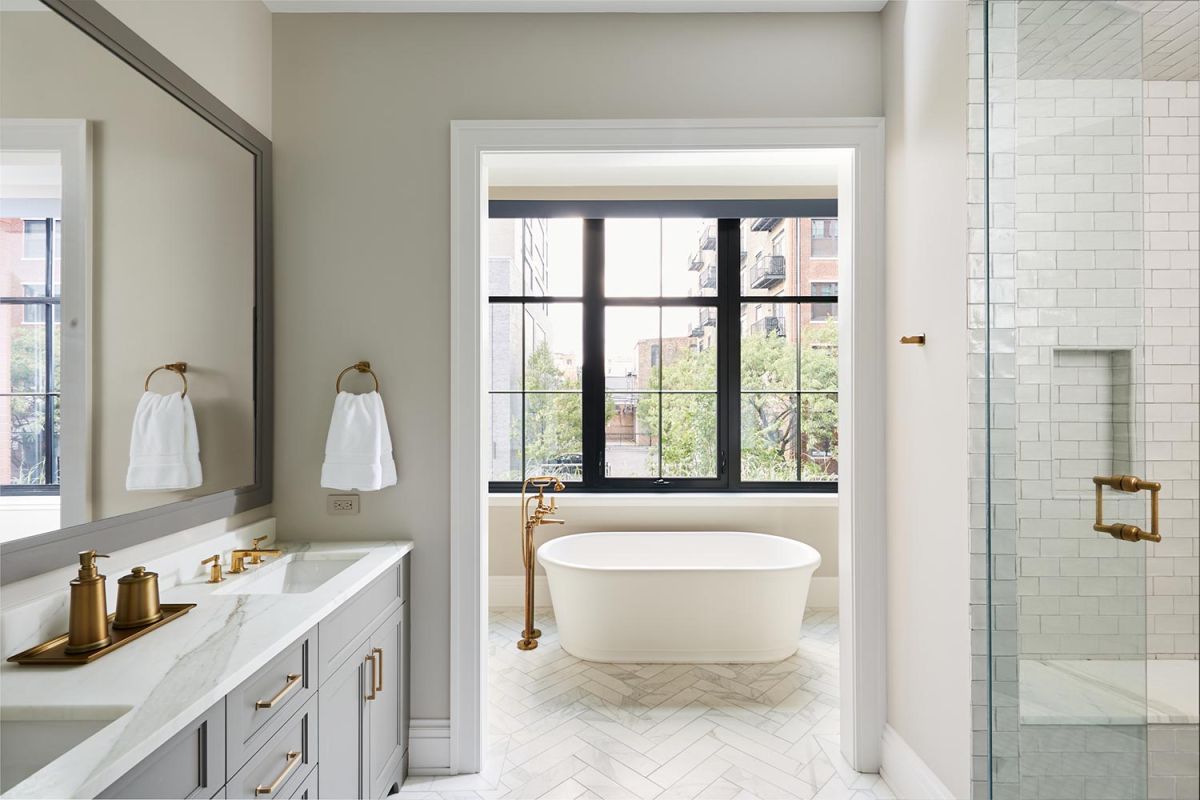 Bright bathroom with freestanding tub, gold fixtures, and large windows
