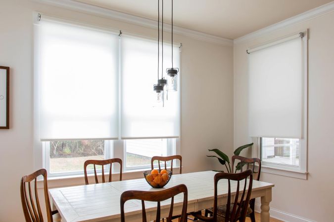 Bright dining room with white roller shades and a farmhouse-style table.
