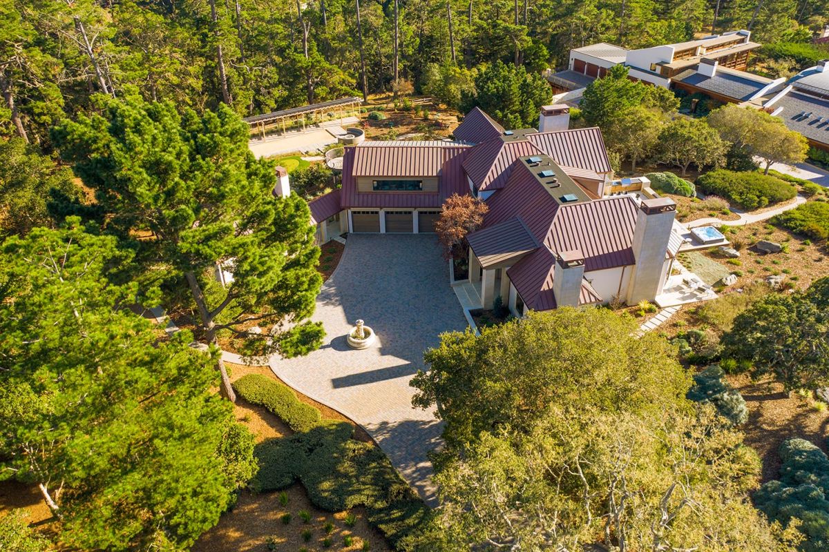 Driveway entrance of a home with a round fountain and forested surroundings