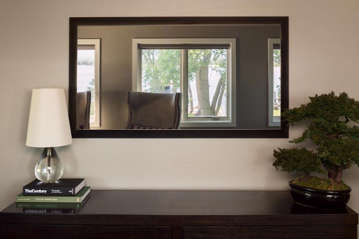 Decorative console with mirror above, bonsai tree, lamp, and stacked books