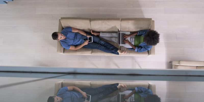 Young multiethnic couple relaxes in the luxury living room, using a tablet and laptop computer top view