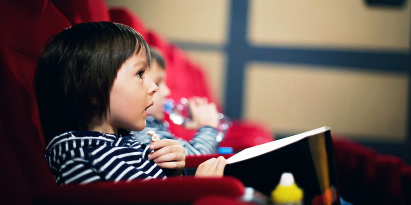 Two preschool children, twin brothers, watching movie in the cinema, eating popcorn