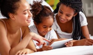 3 girls different ages looking at a paper and smiling together while laying down on stomach