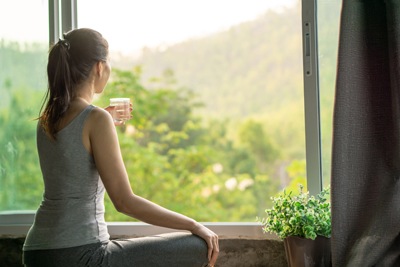 woman looking outside of the window drinking water and relaxing